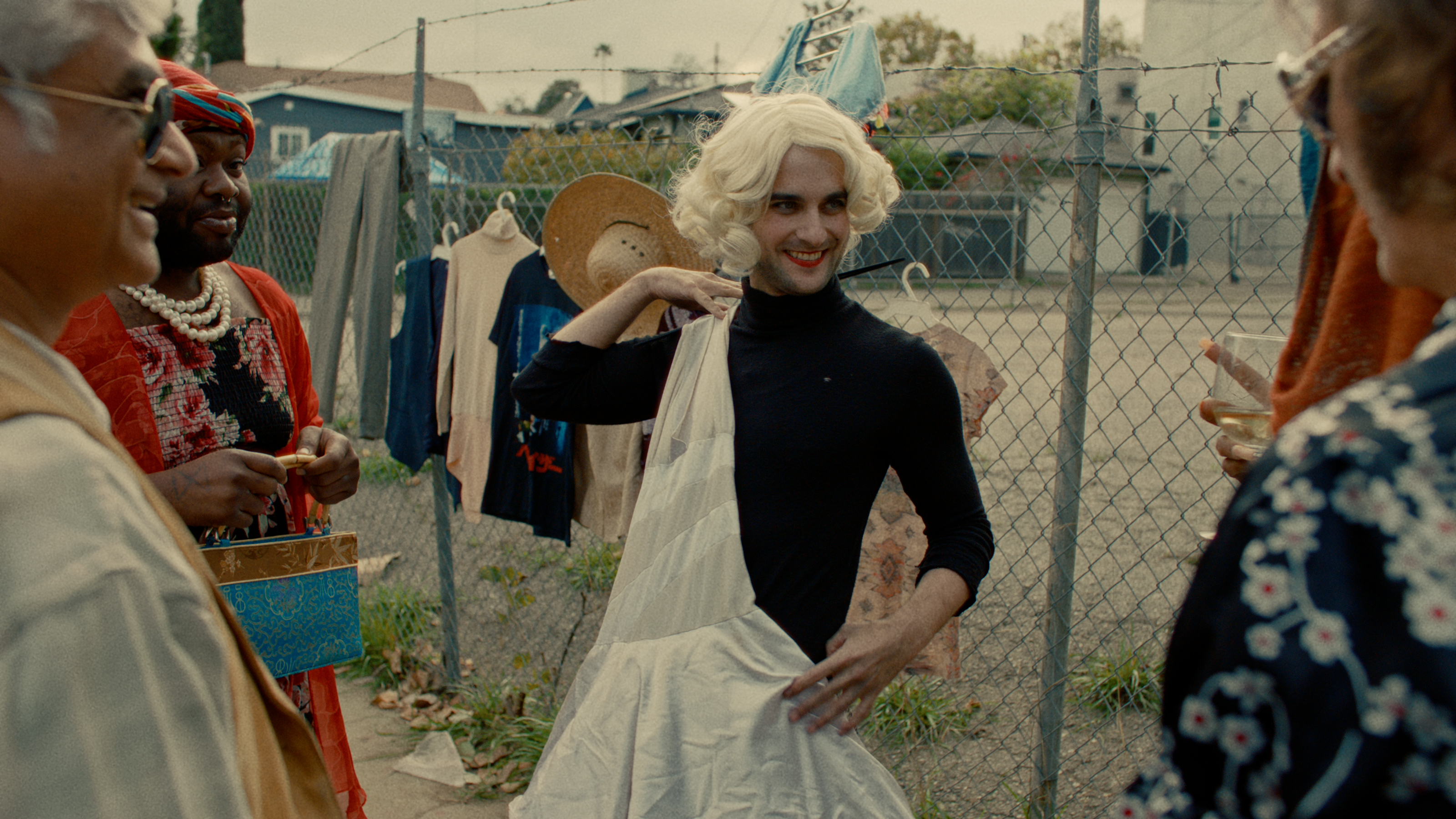 The protagonist holds up a white dress surrounded by colorful community members